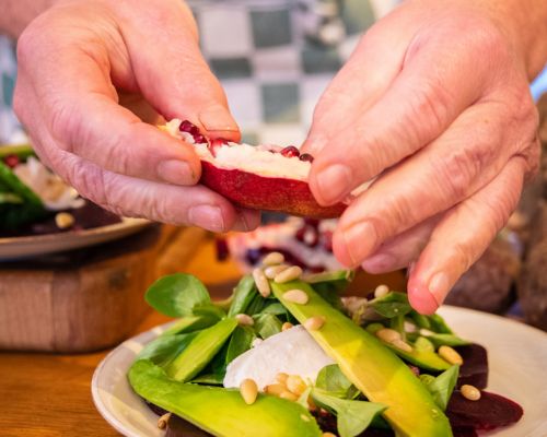 salade avocado twee handen die grannatappel pitten losmaken boven een salade met avocado