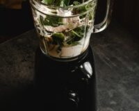 blender Een glazen blender kom gevuld met een wit ingredient en groen blad